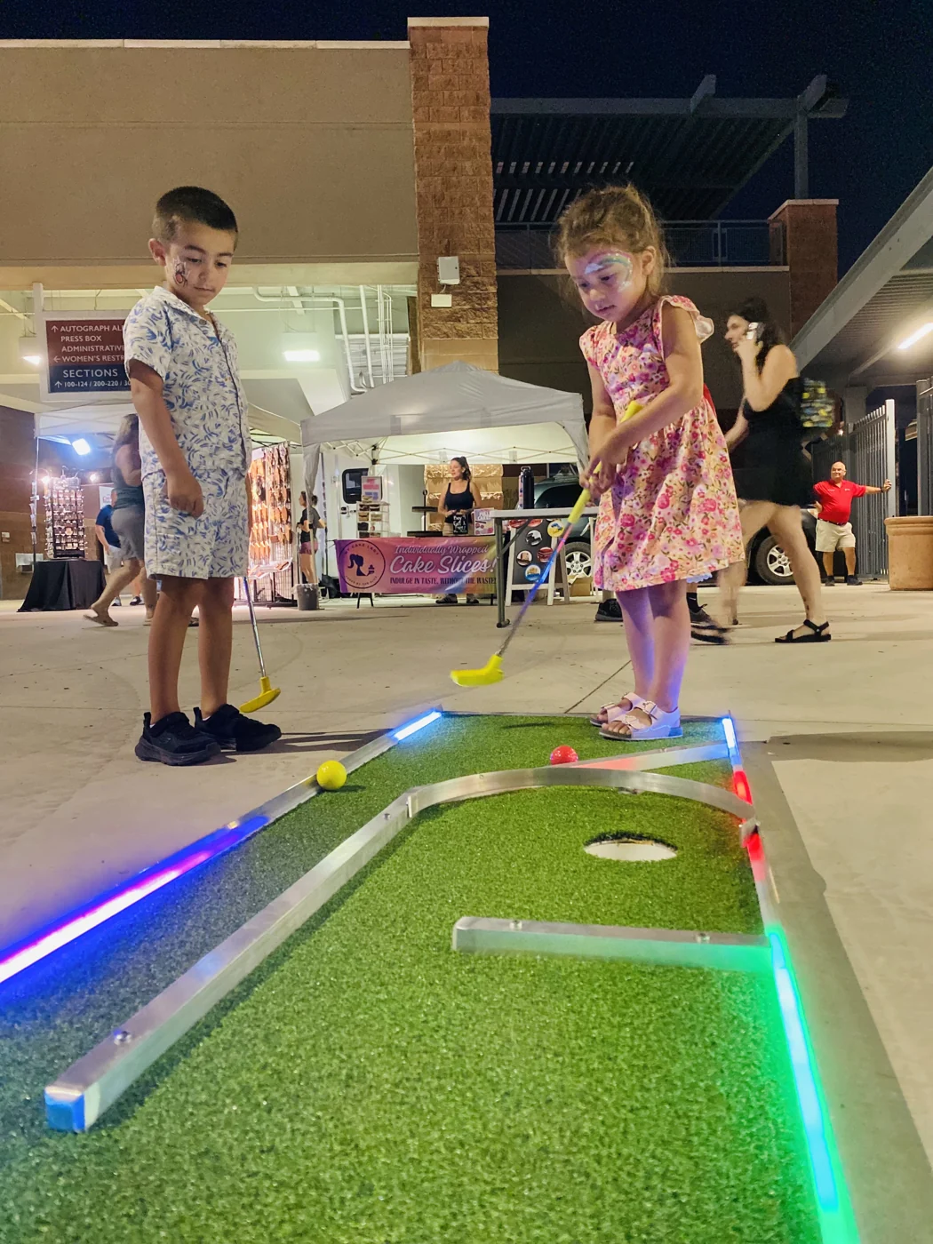 Children playing an illuminated mini golf course at an outdoor event